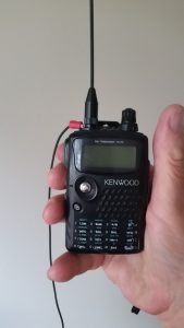 The image shows a person holding a HT radio and comming off the antenna connection base is the rat tail wire ground.